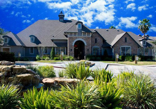 Single-story beige brick clubhouse with tropical landscaping