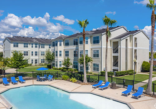 Apartment buildings overlooking pool area with blue chairs and umbrellas