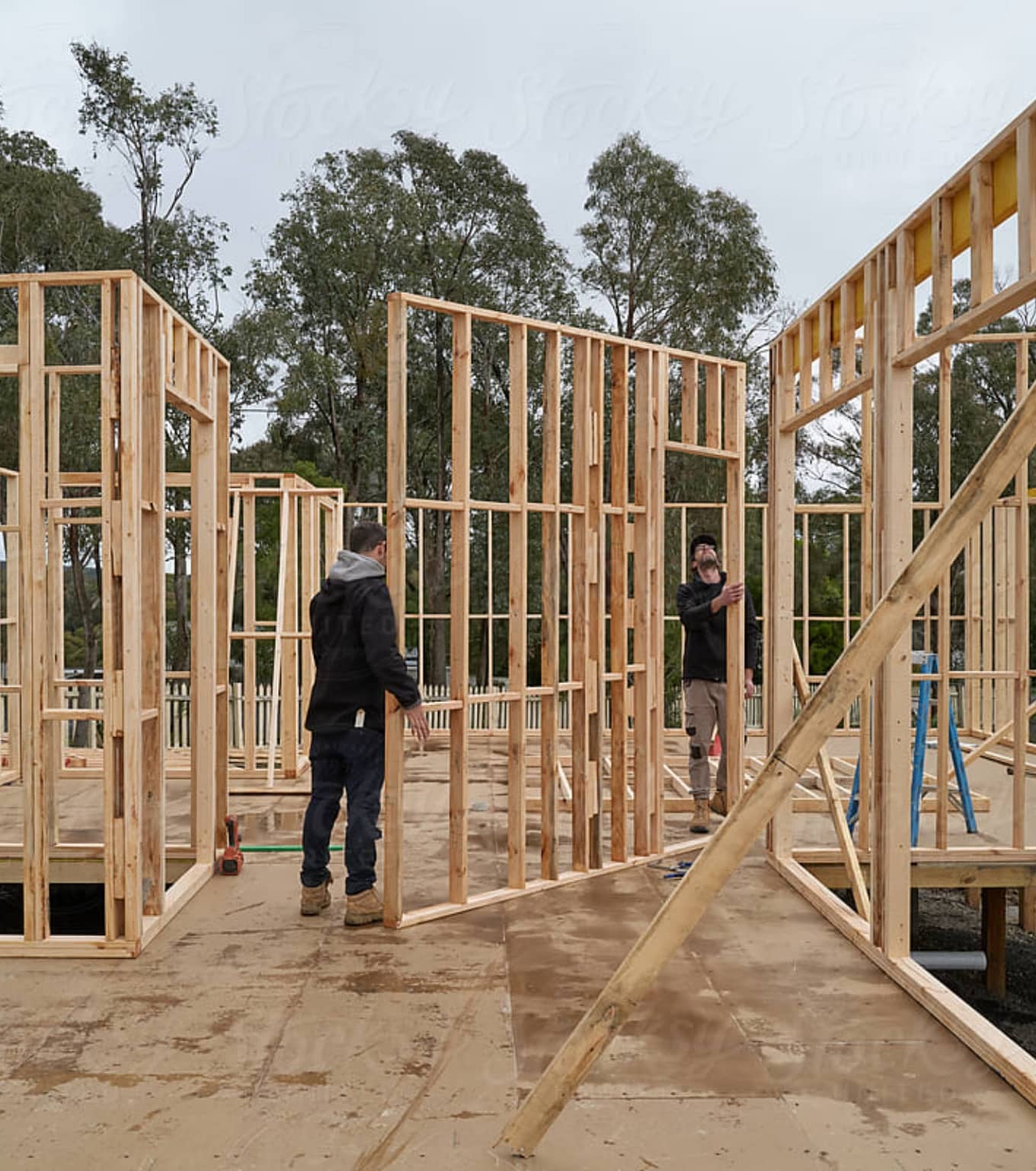 2 men hold a wooden frame while building a house