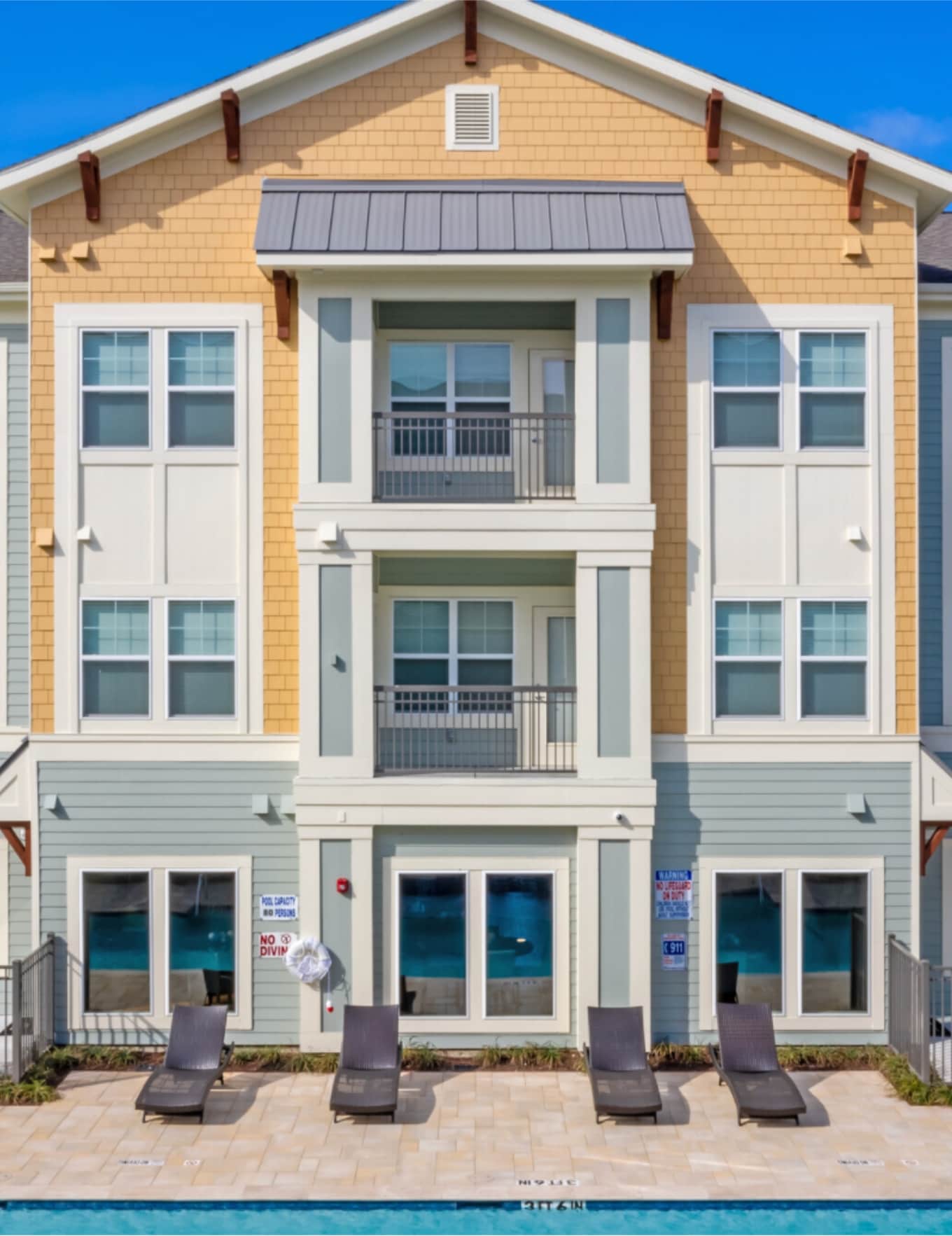 Brightly colored 3-story clubhouse by pool area with lounge chairs