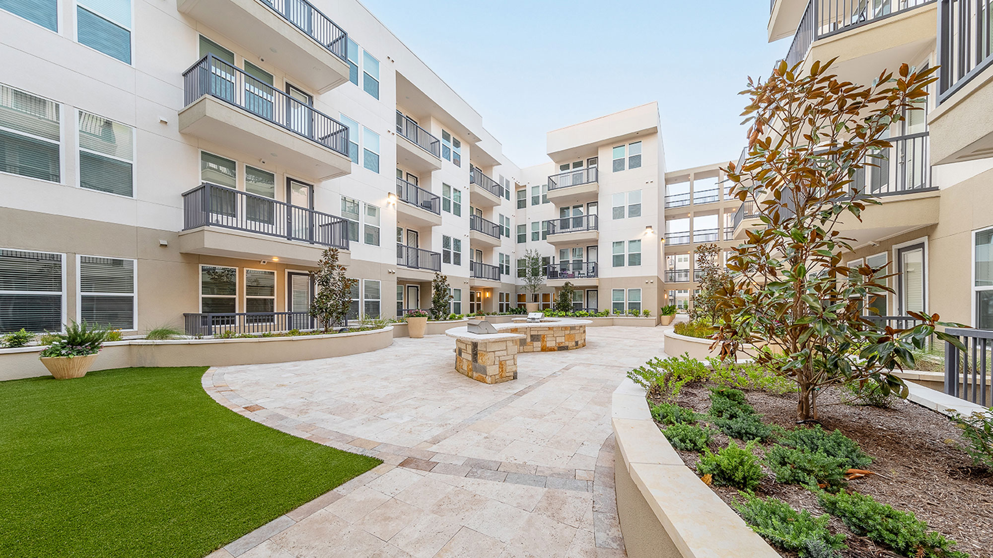 4-story white apartment building connected by stone courtyard with grilling area